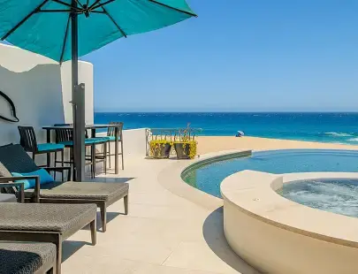 two lounge chairs under an umbrella next to a pool with an ocean view