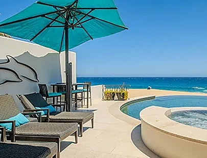 two lounge chairs under an umbrella next to a pool with an ocean view